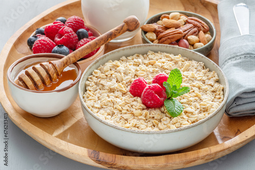 Bowl of porridge or oatmeal with different ingredients on wooden tray. Breakfast serving.