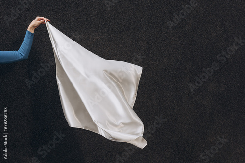 White silk scarf in woman's hand floating on the wind on dark grey background. Lifestyle.