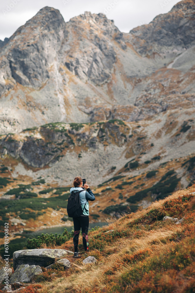 Back view of young woman with backpack standing and take a picture of beautiful Tatra mountains Back view of young woman with backpack standing and take a picture of beautiful Tatra mountains