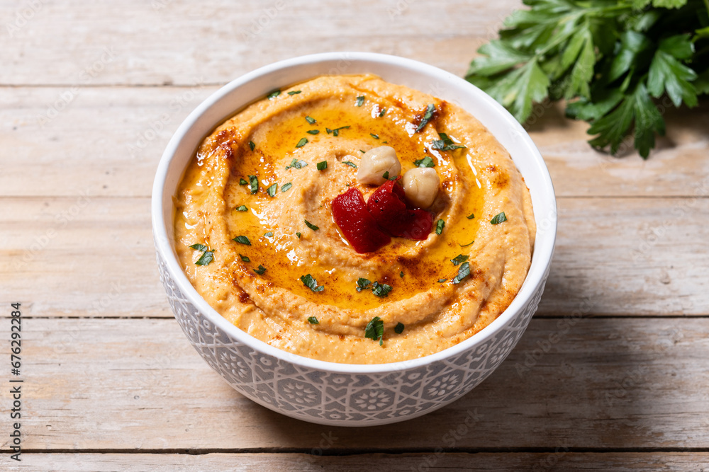 Roasted red pepper hummus in white bowl on wooden table