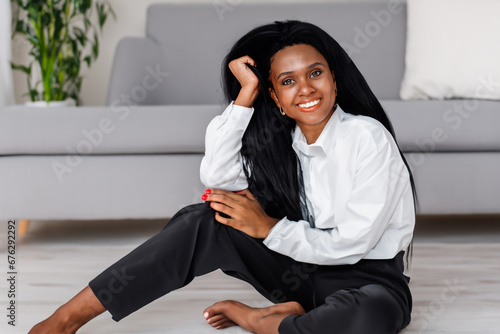 a girl in a white shirt sits on the floor. a young girl with long dark hair sits on the floor near the sofa in a business suit