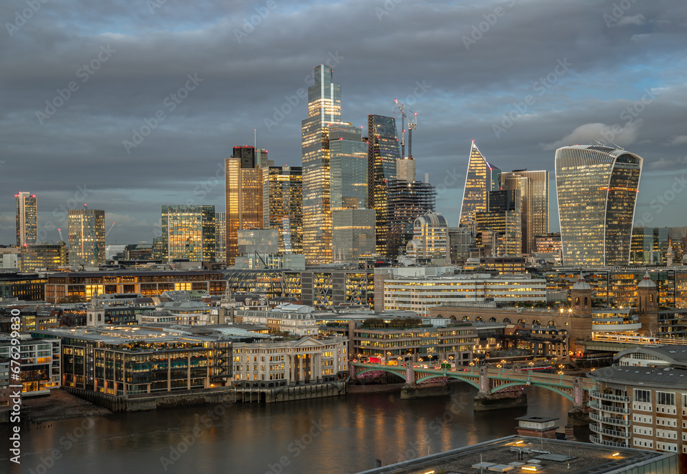 Obraz premium Aerial view of The skyscrapers in the business district of London with the River Thames on foreground at sunset. Architectural modern buildings of the City of London, Space for text, Selective Focus.