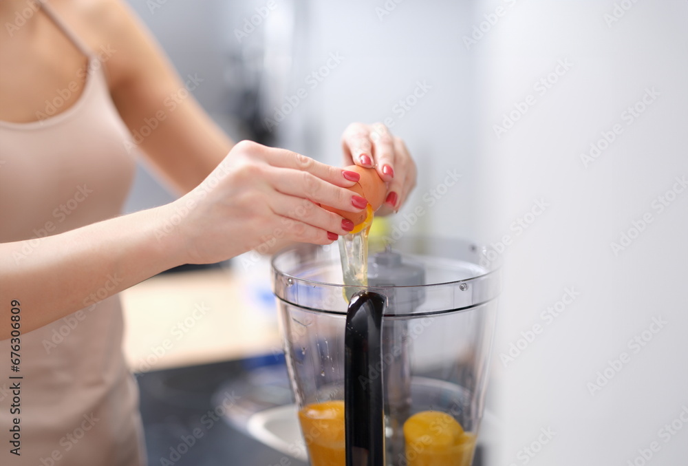 Woman adds eggs to blender for dough. Multicombine for cooking food at home concept Woman adds eggs to blender for dough. Multicombine for cooking food at home concept
