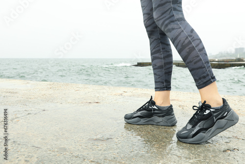 Female legs in leggings and sneakers on sea pier, space for text