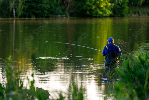 Middle aged fisher-man standing with fishing rod in the pond