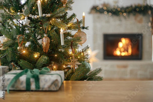 Cuadro en lienzo Merry Christmas! Stylish christmas decorated tree, golden lights, gift on table and burning fireplace