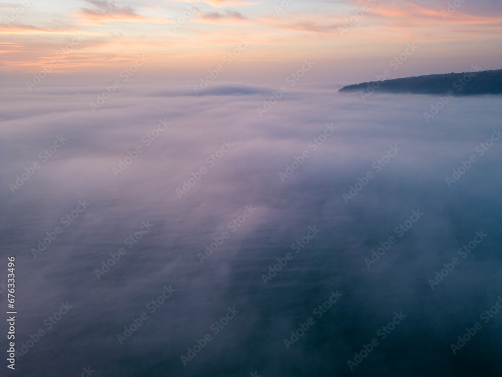 Aerial view of a sunrise sea with a blanket of morning fog and morning sunbeams shining through