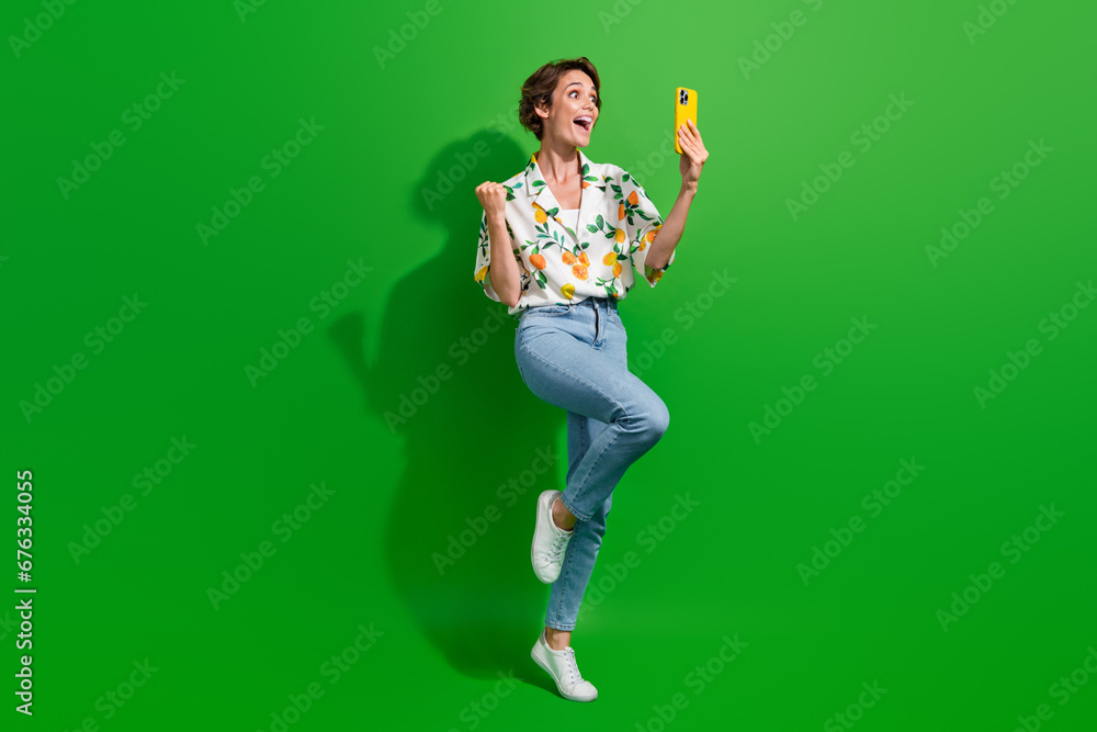 Full body photo of overjoyed young girl raised fist up using smartphone receive email approved new job isolated on green color background Full body photo of overjoyed young girl raised fist up using smartphone receive email approved new job isolated on green color background