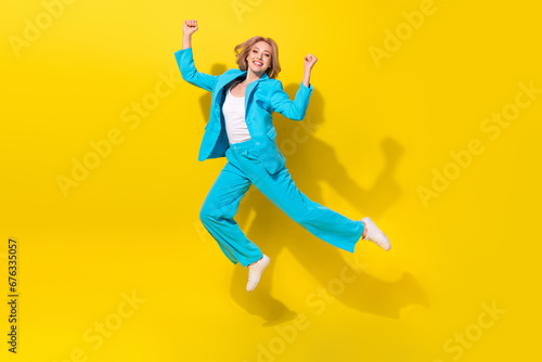 Full length photo of positive satisfied woman wear blue stylish suit clenching fists flying win lottery isolated on yellow background © deagreez