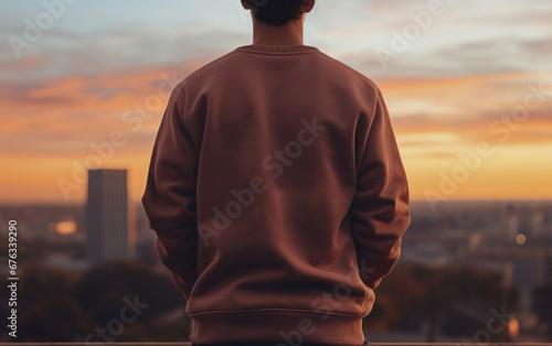 Back view of a man wearing sweatshirt standing on a high place with sky and city blurred background photo