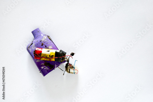 The remains of a discarded dirty muddy neon coloured electronic cigarette vape, and its internal components and battery. Shot above a white paper background.