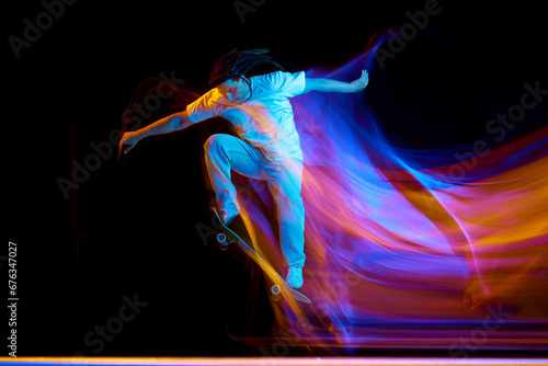 Man skateboarder performing freestyle tricks in motion isolated black studio background in mixed neon flashes of light. Concept of youth culture.