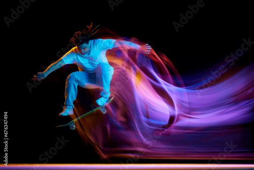 Foto Young man, skateboarder doing jumps tricks with neon motion blur isolated black studio background