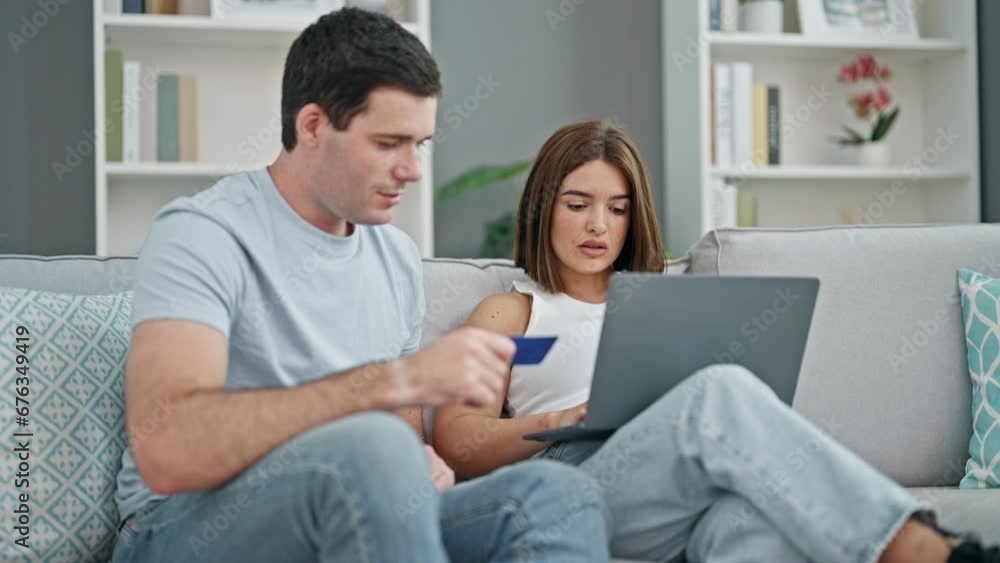 Beautiful couple shopping with laptop and credit card sitting on sofa smiling at home Beautiful couple shopping with laptop and credit card sitting on sofa smiling at home