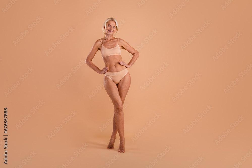 Fototapeta premium Full length photo of charming sweet senior lady dressed lingerie walking empty space isolated beige color background