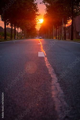 This picturesque scene features the sun rising over an open asphalt road, set in the European countryside. The image perfectly captures the tranquil beauty of a sunny morning or evening, reflecting © Bjorn B