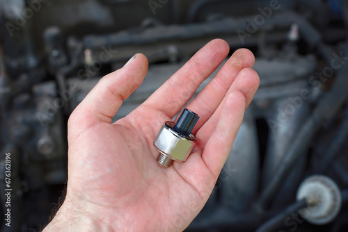 Hand with new knock sensor for broken car engine. Installing new electrical spare part. Replacing faulty knock sensor, engine problems. Car maintenance. Selective focus