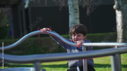 Child playing at playground carousel during autumn season. Little boy spinning in circles while holding on metal bar getting exercise and outdoor activity