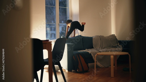 Candid small boy running and jumping on top of sofa couch at night, energetic kid having fun by himself at home