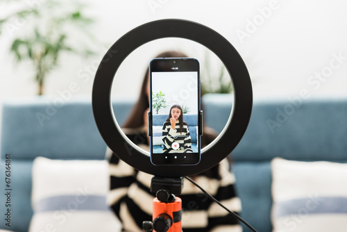 Young woman sitting on couch and recording podcast on smartphone