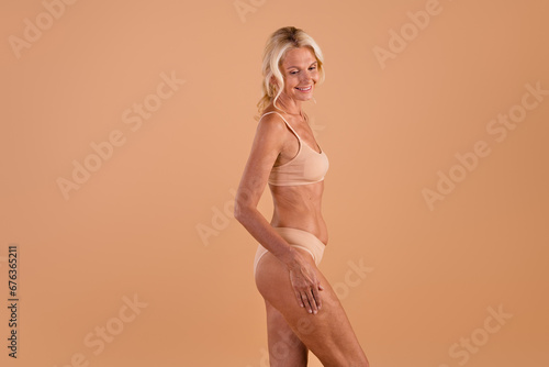 Profile side photo of gorgeous grandmother touch hips chin pose dressed stylish lingerie isolated on beige color background