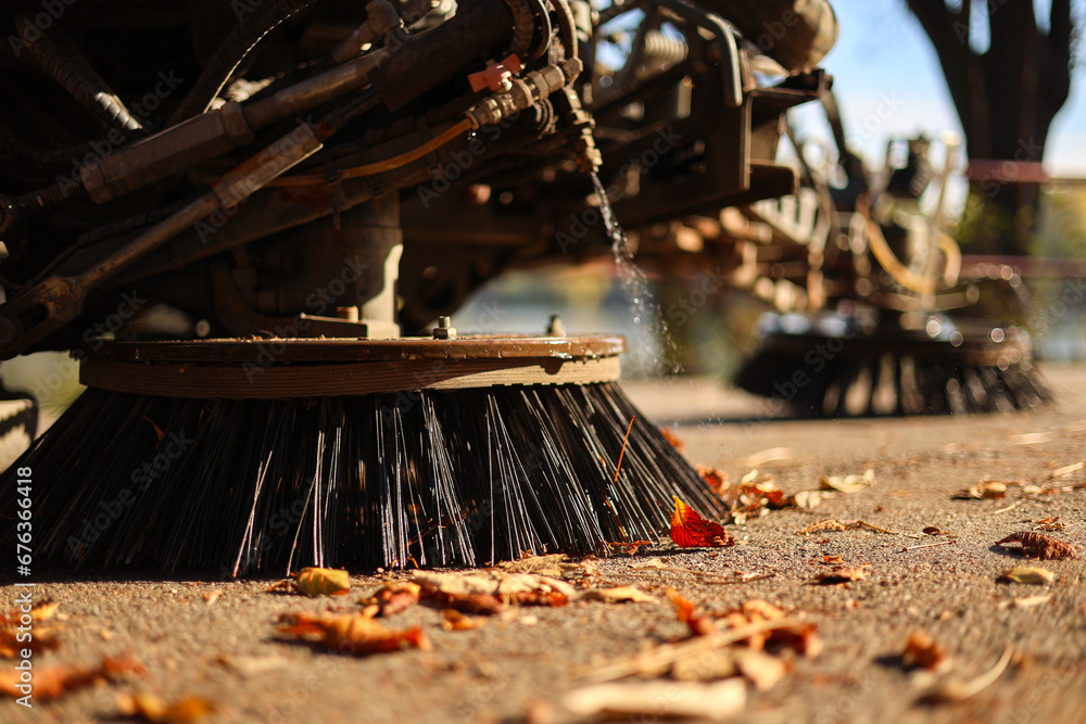 Cleaning the alleys in a park of a lot of fallen autumn leaves on the asphalt. Close up photo with a street utility car machine used to clean the public parks.