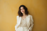 Portrait of a mysterious brunette in a white summer suit leaning against a yellow wall with copy space.