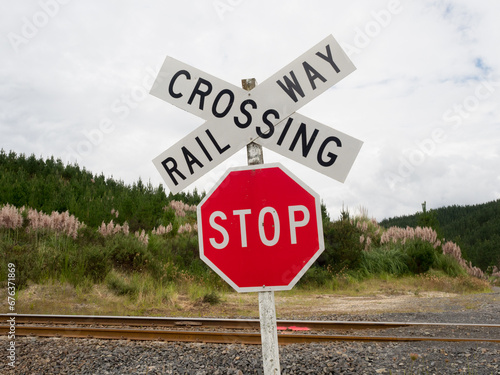 A red stop sign and railway crossing sign in wild landscape with rail track visible.New Zealand