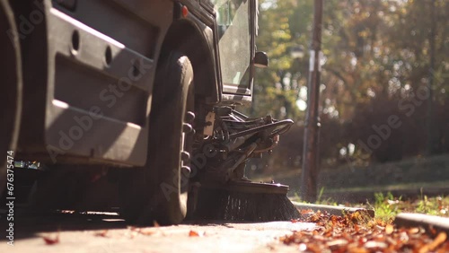 Park maintenance during autumn. Close up 4k video with an industrial vehicle with two big brushes cleaning the alleys from a park of fallen autumn leaves on the ground. selective focus.
