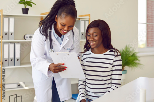 Happy African American female doctor and patient looking at some documents on clipboard. Smiling young woman together with her physician looking at medical report files on clip board photo