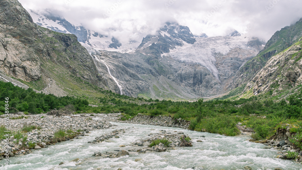 Obraz premium The bubbling clear water of a mountain river with large stones high in the mountains. Clean water flows down from a glacier in the mountains. Landscape in the mountains. Uncontaminated environment.