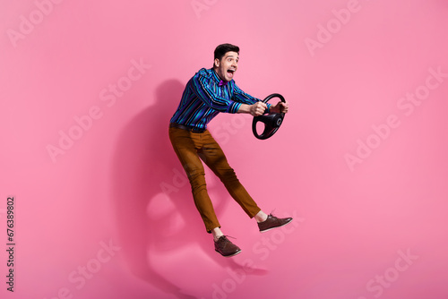 Full length photo of funky young driver jumping holding steering wheel high speed transportation isolated on pink color background