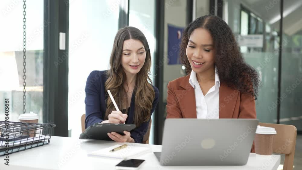 African female office worker and her blonde colleague are discussing financial reports. Indoor shot of two young businesswomen talking about company accounting analysis African female office worker and her blonde colleague are discussing financial reports. Indoor shot of two young businesswomen talking about company accounting analysis