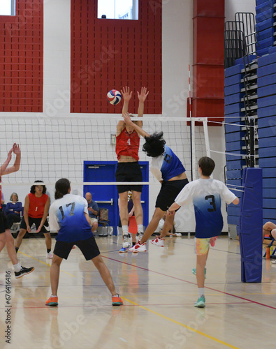 Short volleyball player hits around tall blocker photo