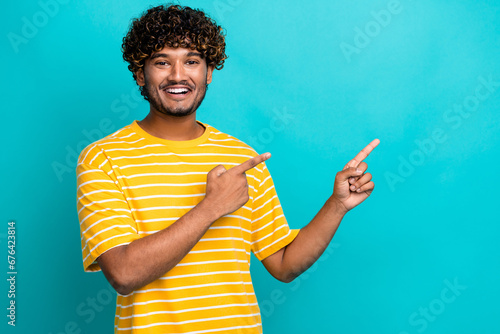 Photo portrait of nice young male pointing empty space dressed stylish striped yellow garment isolated on cyan color background