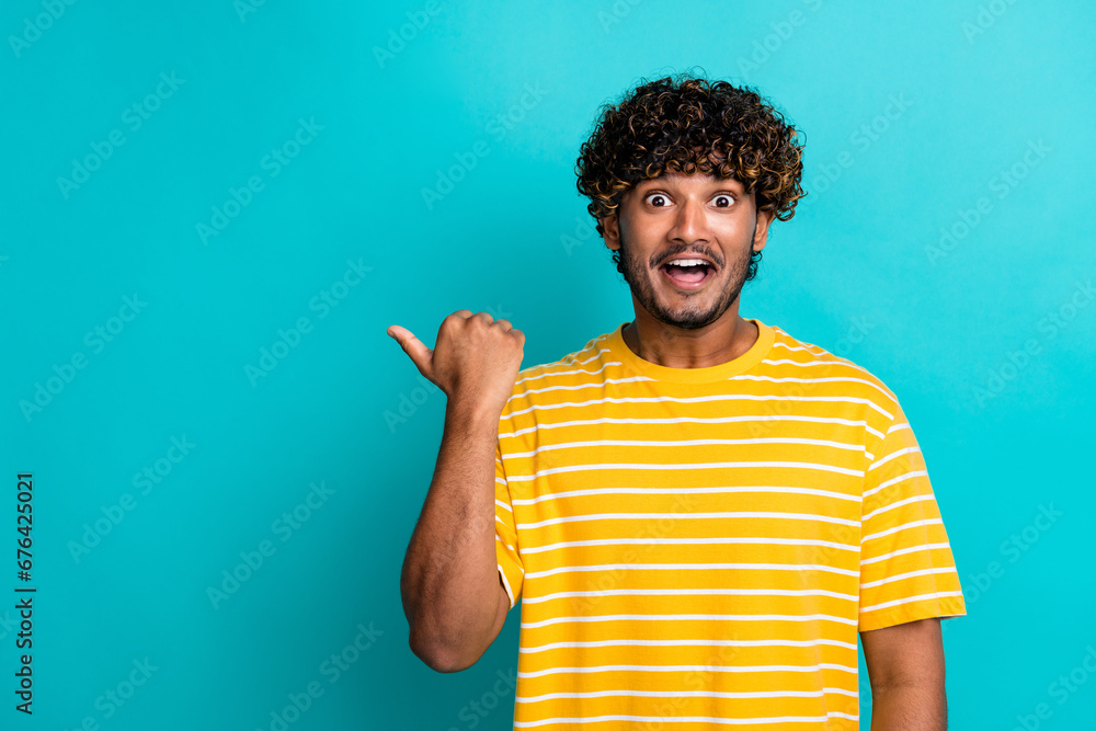 Photo portrait of nice young male point impressed empty space dressed stylish striped yellow garment isolated on cyan color background Photo portrait of nice young male point impressed empty space dressed stylish striped yellow garment isolated on cyan color background
