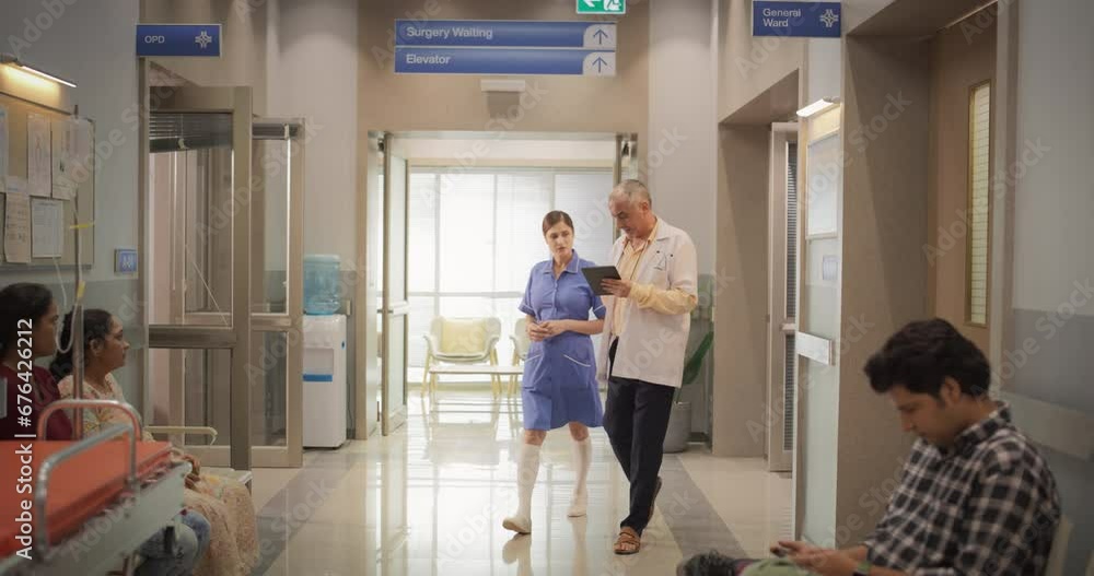 Slow Motion Portrait of Indian Male Doctor and Female Nurse Walking in Hospital Corridor and Talking while Using a Digital Tablet. Medical Specialists Sharing Notes and Instructions Slow Motion Portrait of Indian Male Doctor and Female Nurse Walking in Hospital Corridor and Talking while Using a Digital Tablet. Medical Specialists Sharing Notes and Instructions