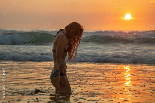 Beautiful girl on the seashore. Colorful sunset. Waves on the water. Sunny evening.