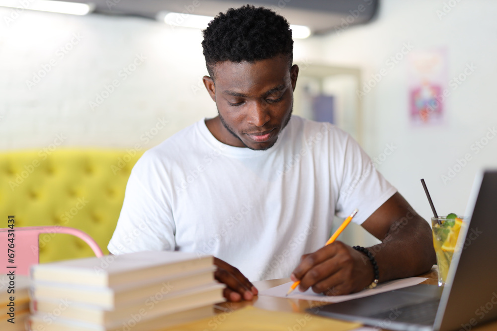 Serious young man, a student, sitting at a desk in a university setting, studying with a laptop and books. Serious young man, a student, sitting at a desk in a university setting, studying with a laptop and books.