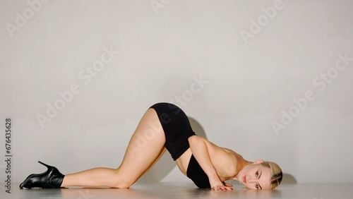 In the frame on a gray background. Woman, she lies behind her shadow, lifting the buttocks up on her open clothes and high heels. Shows dance movement, poses. Shes sexy, attractive, plastic