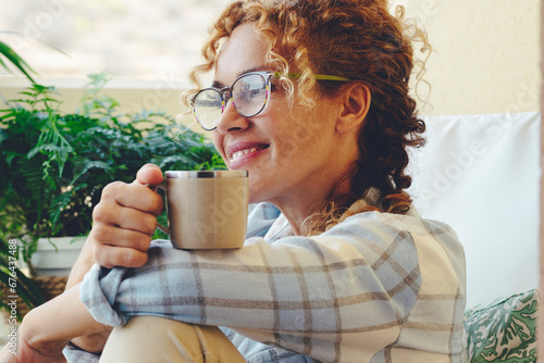 Adult woman smile sitting on the lounge chair and have relax time drinking cup of coffee or tea. Happy relaxed lifestyle for female people with eyeglasses