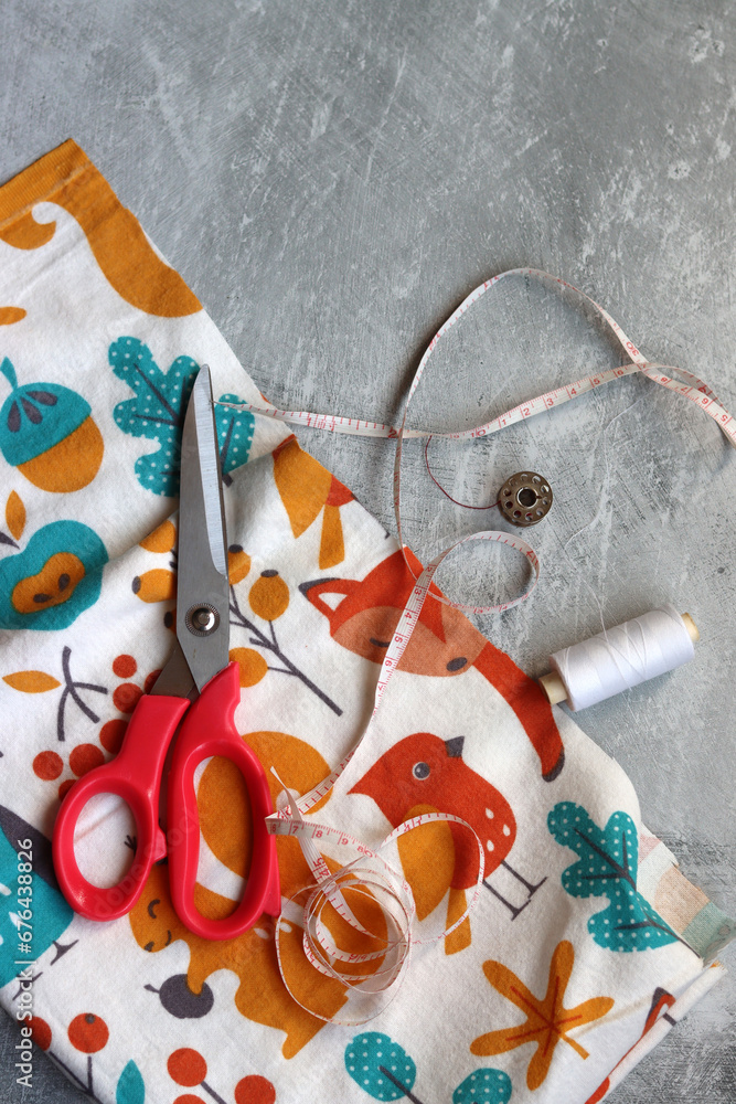 Obraz premium Sewing tools: scissors, thread, fabric, pins, buttons and colorful soft cotton fabric on grey background with copy space Flat lay composition with sewing accessories 