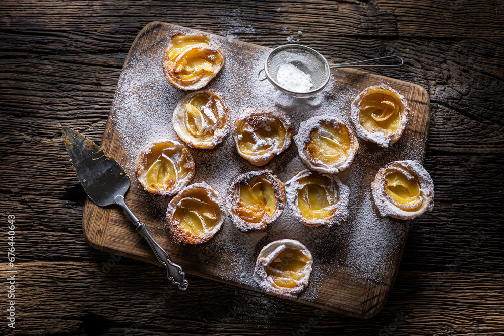 Mini tarts made of puff pastry and sliced apples sprinkled with powdered sugar on wooden cutting board Mini tarts made of puff pastry and sliced apples sprinkled with powdered sugar on wooden cutting board
