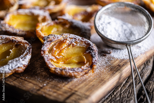 Mini tarts made of puff pastry and sliced apples sprinkled with powdered sugar on wooden cutting board photo