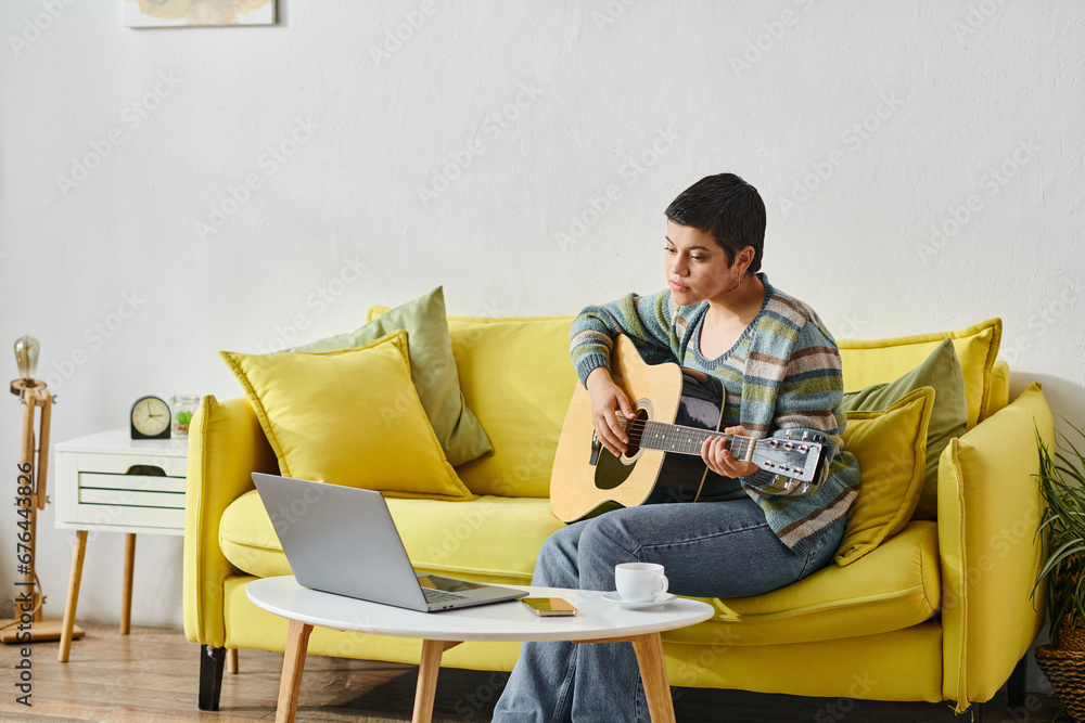 focused attractive woman in casual attire learning how to play guitar on remote music lesson