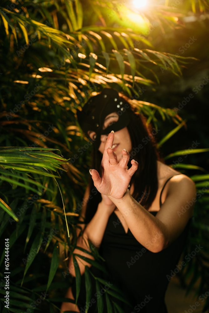 Sexy woman in a BDSM cat mask posing in a tropical garden among palm trees. BDSM concept. Sexy woman in a BDSM cat mask posing in a tropical garden among palm trees. BDSM concept.