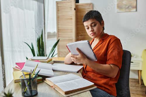 attractive young student looking attentively at her notes sitting at desk, education at home photo