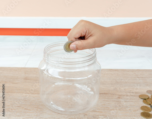 Child hand putting coin into plastic money bottle or piggy bank. Concept of saving money for the future or money growth