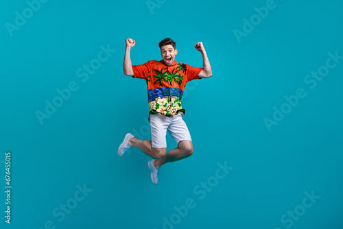 Full body photo of funky jumping crazy guy fists wear tropics shirt celebrate summertime season hooray isolated on blue color background