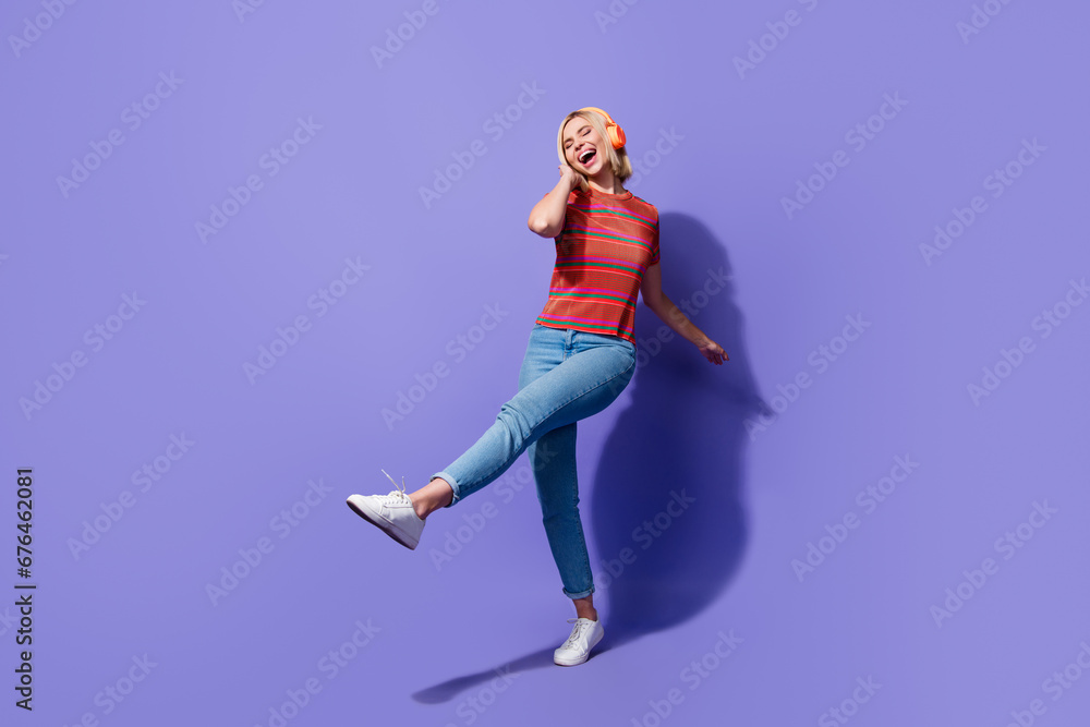 Full body photo of hipster girl in denim jeans red t shirt listen headphones dancing touch headphones isolated on purple color background